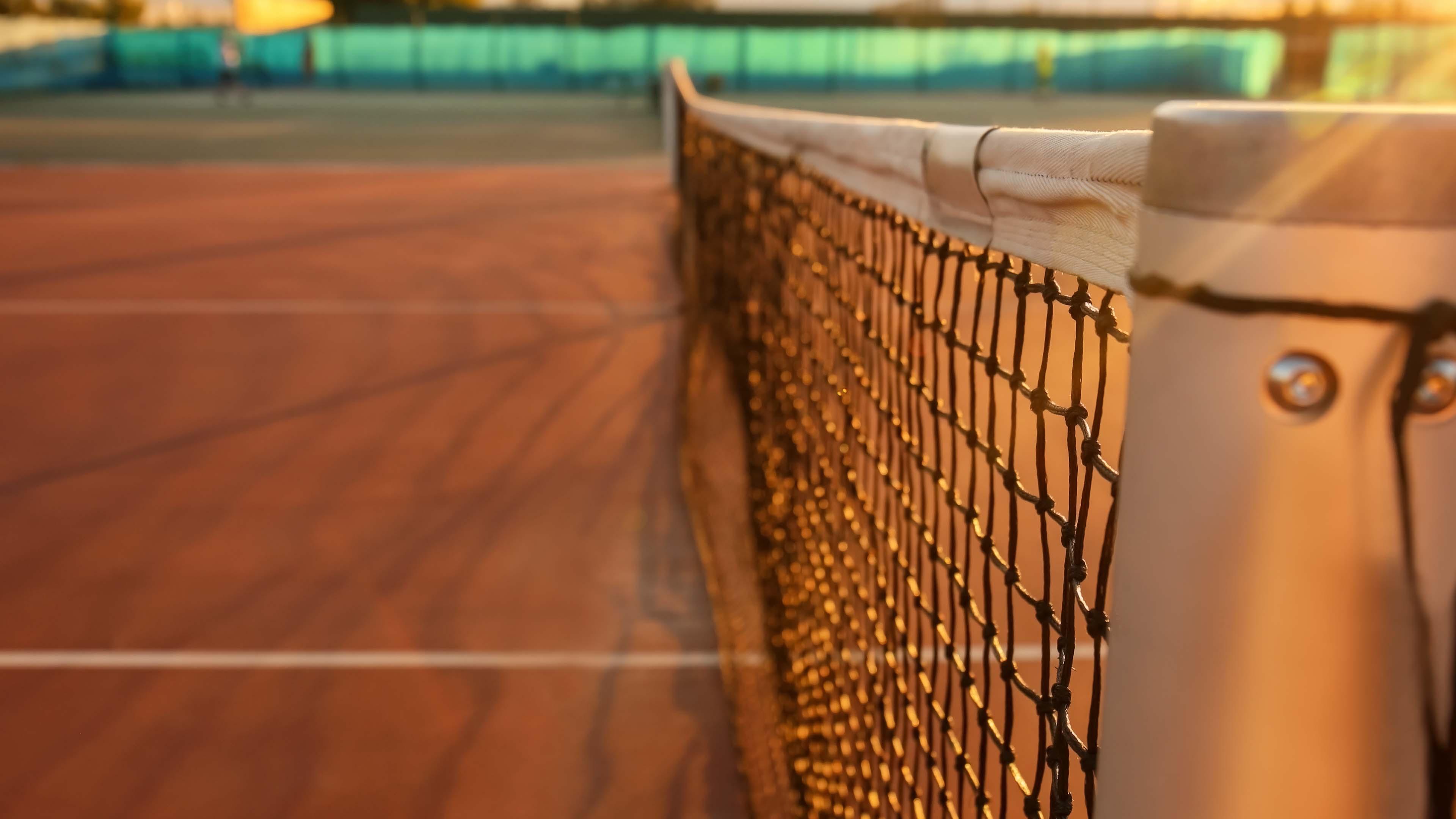 Tennis net on a clay court at sunset